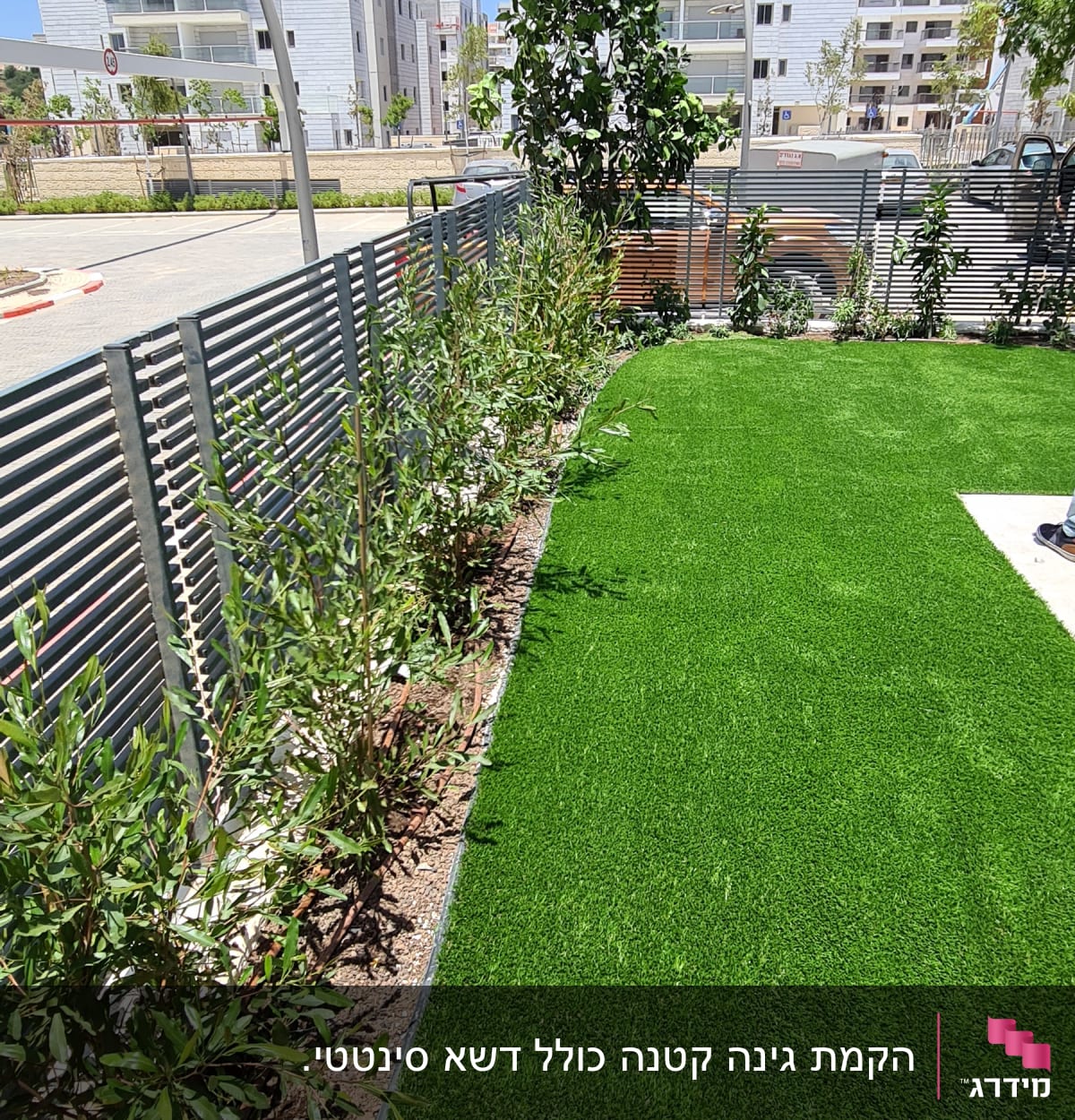 דשא ירוק עם שיחים לאורך גדר מתכת